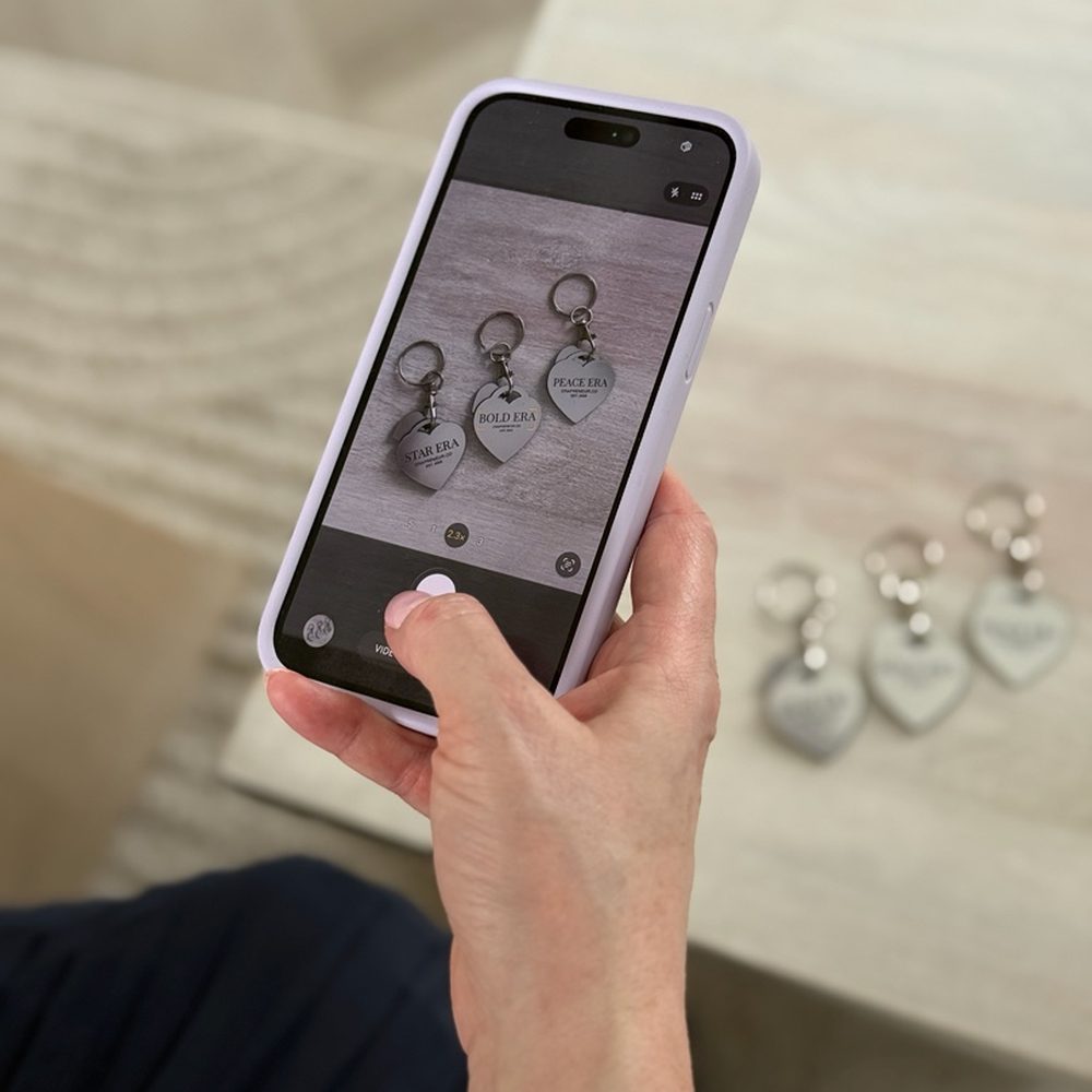 A hand holding a phone photographing Era heart keychains